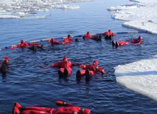 Pessoas usam roupas vermelhas de neoprene e flutuam em lago no gelo