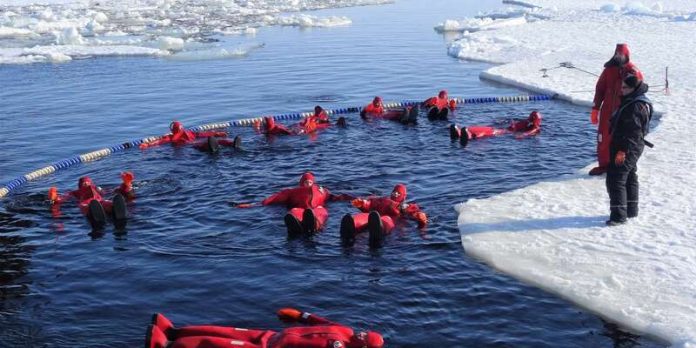 Flutuar em lago congelado na Lapónia Pessoas usam roupas vermelhas de neoprene e flutuam em lago no gelo