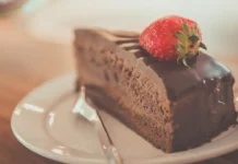 20 curiosidades sobre o bolo de chocolate que explicam o seu sabor e textura Illustrative photograph. It does not confirm the identity of any person mentioned in the article. Close-up of a delectable chocolate cake slice topped with a fresh strawberry on a plate.