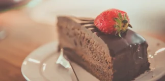 20 curiosidades sobre o bolo de chocolate que explicam o seu sabor e textura Illustrative photograph. It does not confirm the identity of any person mentioned in the article. Close-up of a delectable chocolate cake slice topped with a fresh strawberry on a plate.