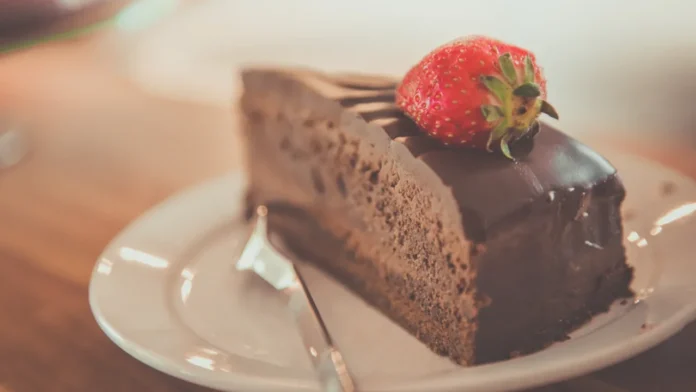 20-curiosidades-sobre-o-bolo-de-chocolate-que-explicam-o-seu-sabor-e-textura Illustrative photograph. It does not confirm the identity of any person mentioned in the article. Close-up of a delectable chocolate cake slice topped with a fresh strawberry on a plate.