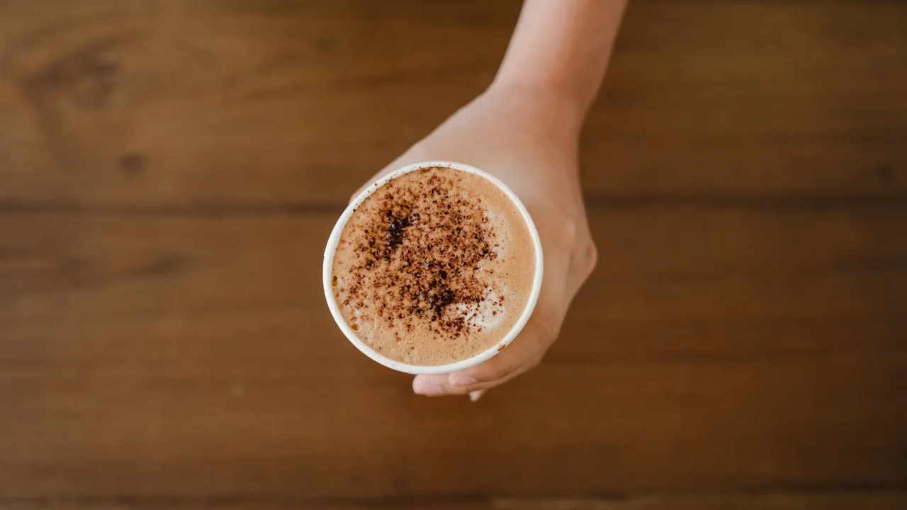 Illustrative photograph. It does not confirm the identity of any person mentioned in the article. A hand holding a cappuccino cup topped with cocoa powder, captured from above.