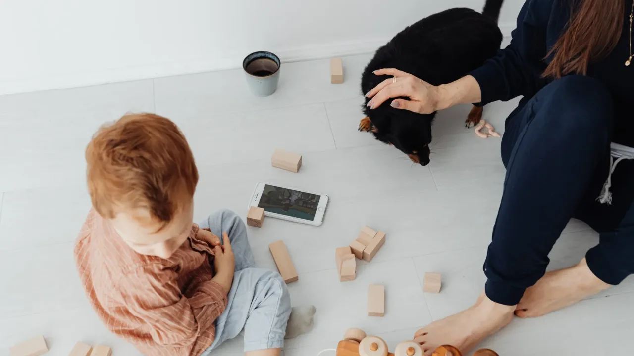Illustrative photograph. It does not confirm the identity of any person mentioned in the article. A child playing with wooden blocks alongside a pet dog and adult, creating a warm family atmosphere.